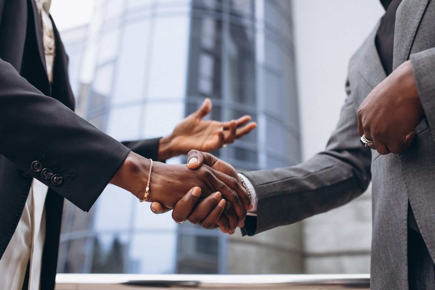 Two business people shaking hands in front of a glass office building